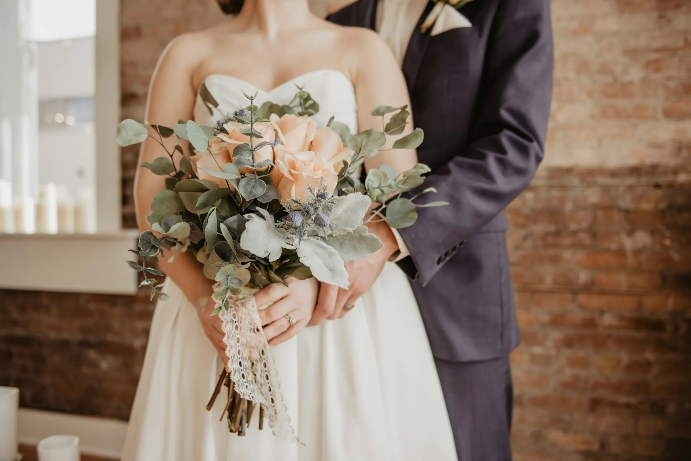 Close-up of a bride in a white dress with pearl details, hands gracefully clasped.