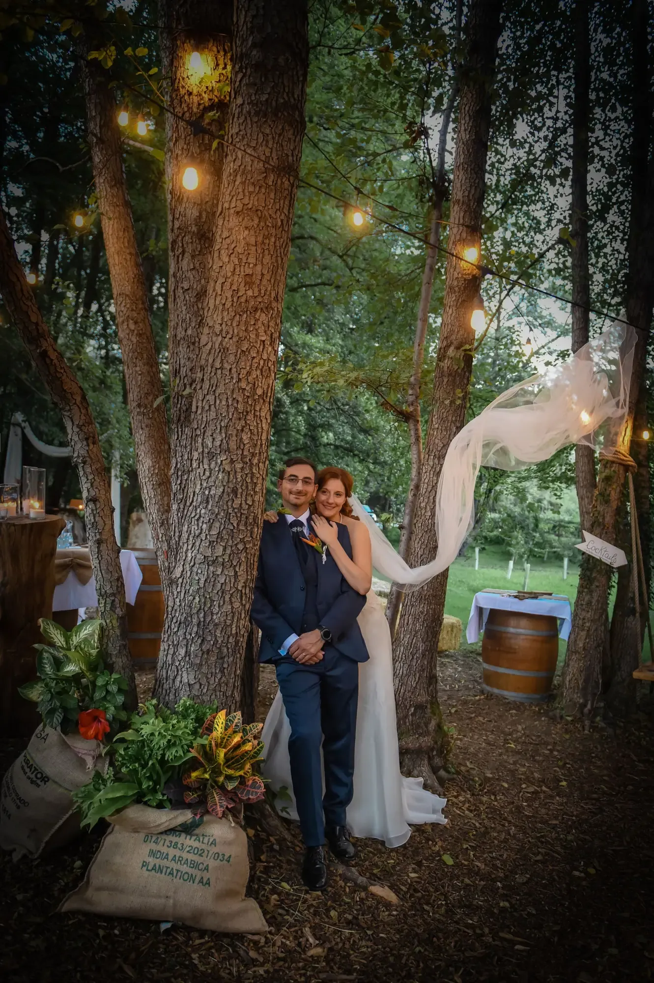 A bride and groom embrace outdoors under enchanting fairy lights.