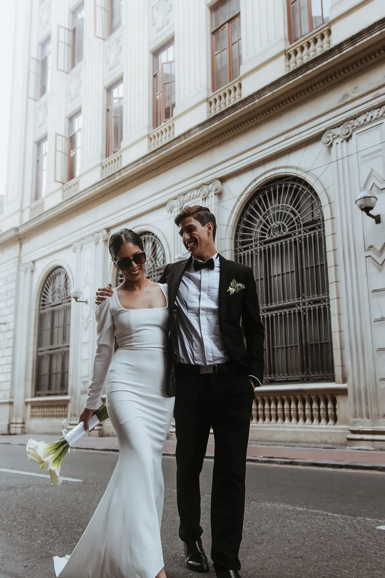 Smiling bride and groom walk arm in arm on Lima's city streets, radiating love and style.