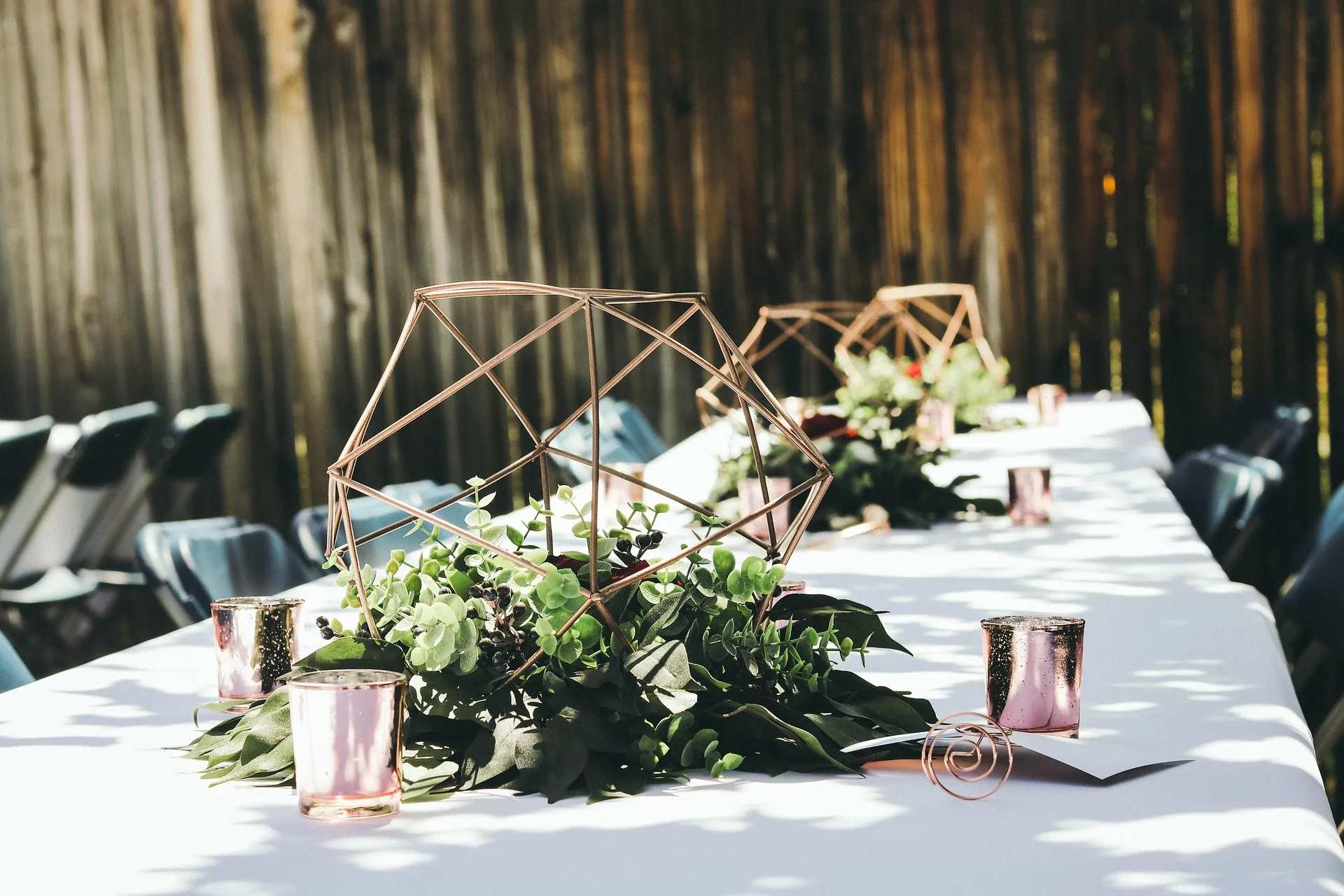 Wedding reception table with geometric floral centrepieces and rose-coloured candle holders.