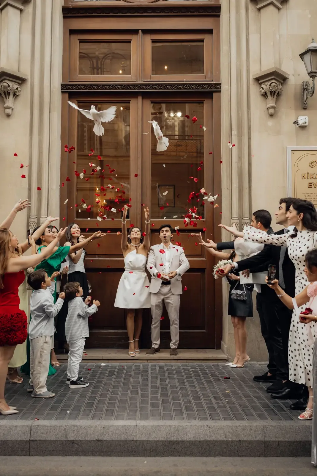 Bride and groom celebrate wedding exit with guests, doves, and rose petals.