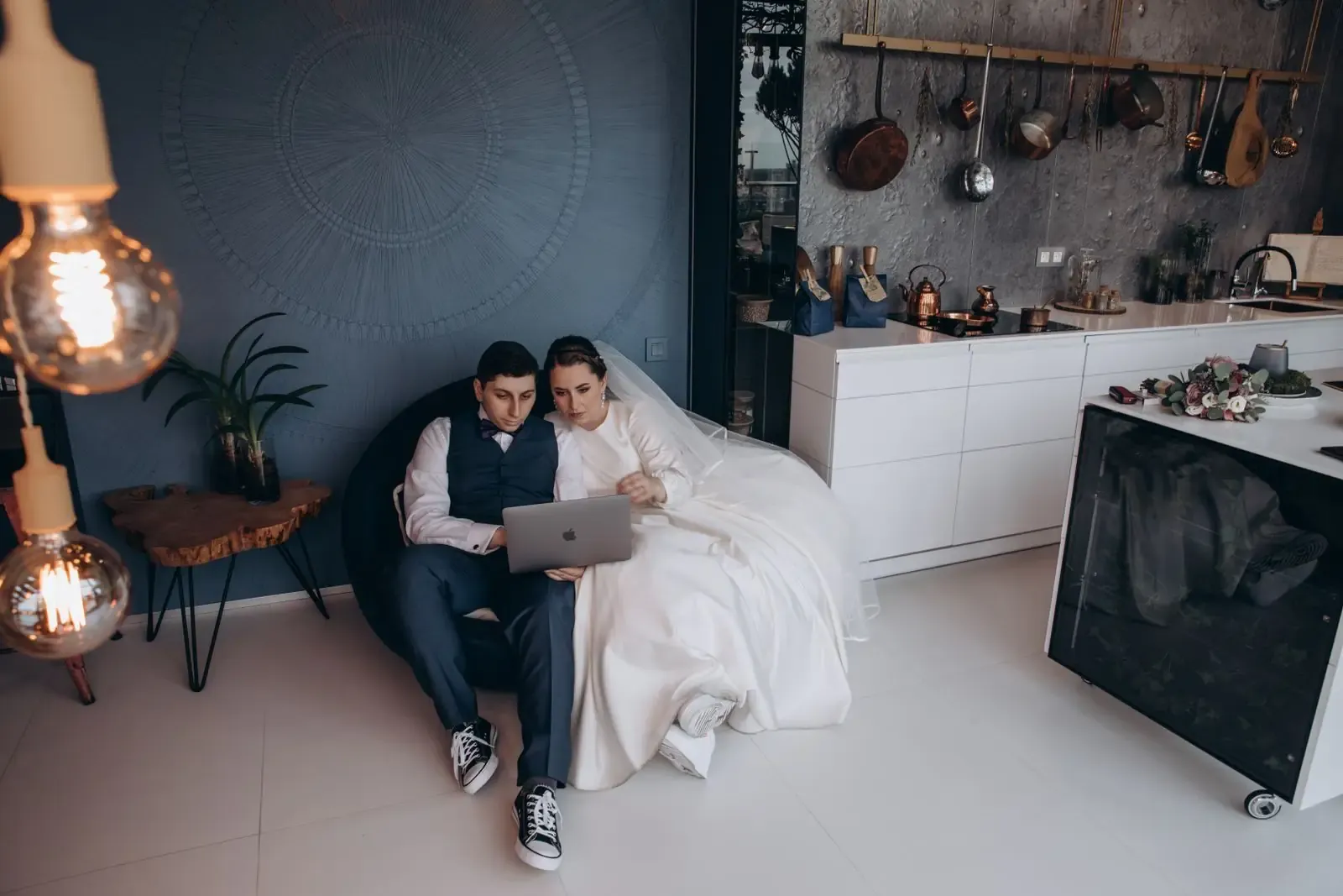 Bride and groom at a kitchen table, looking at a laptop together.