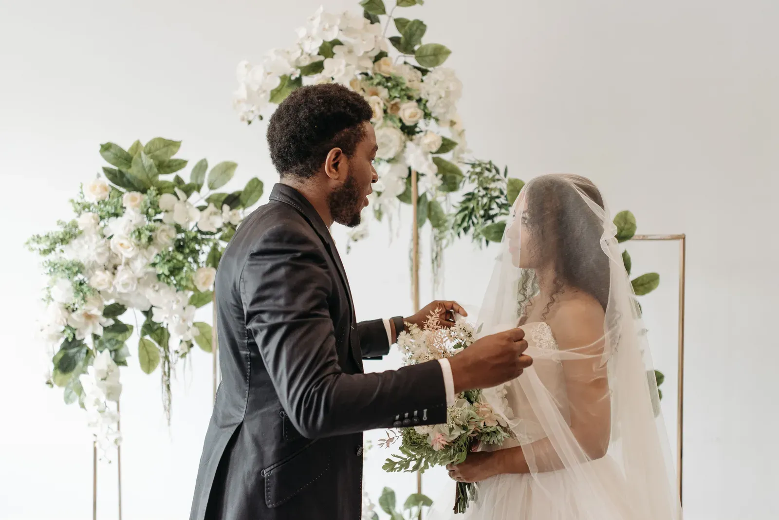 The groom lifting the bride's veil under an arch of white flowers.