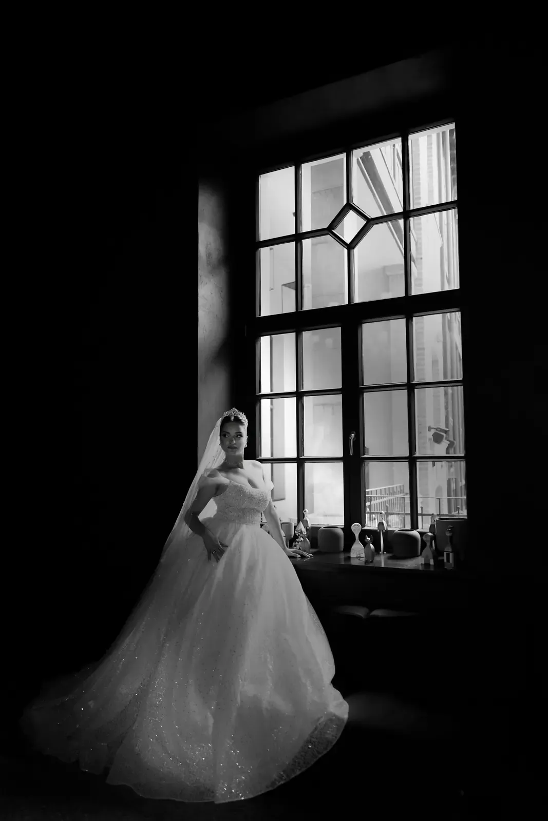 A stunning black and white bridal portrait capturing elegance and grace by a window.