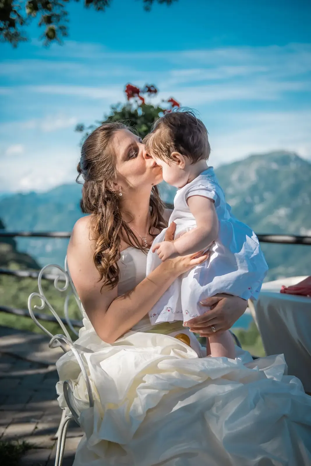 A beautiful bride kisses her child in a picturesque outdoor setting in Barni, Italy.