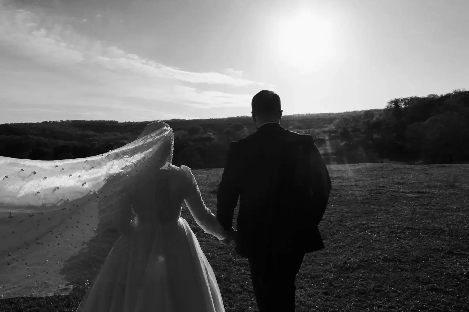 A wedding couple walking together in bright sun, in black and white.