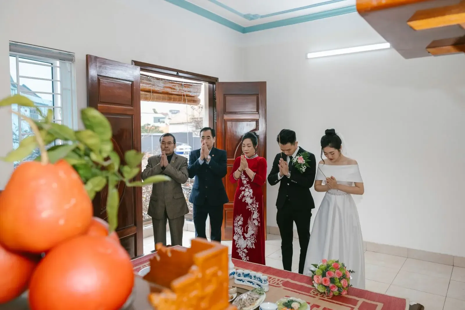 A group participating in a traditional wedding ceremony with prayers, indoors, featuring vibrant attire and cultural elements.