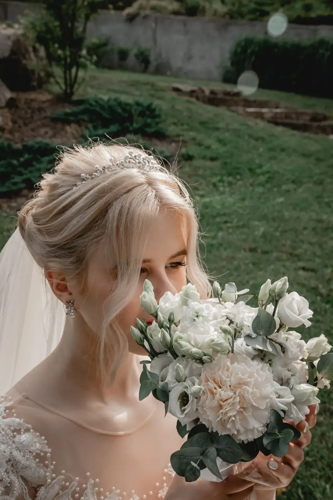 Bride holding a white floral bouquet in a serene outdoor garden setting, summer day.