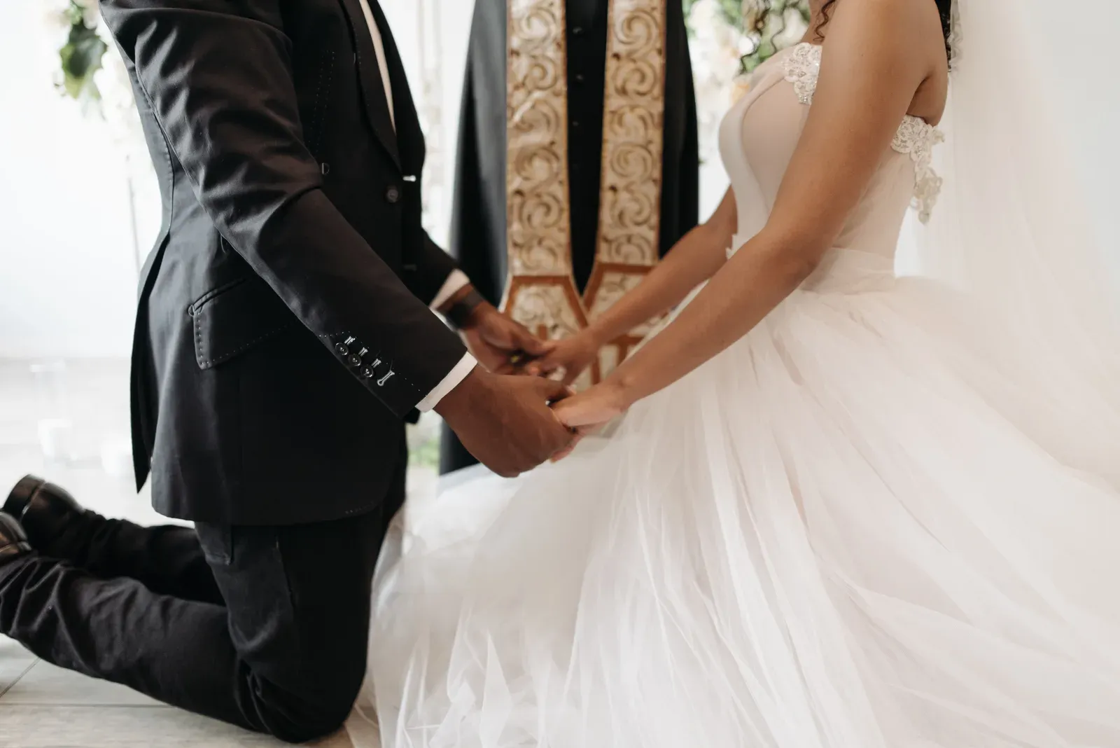 The couple's joined hands at the altar, the pastor's hand resting over theirs.