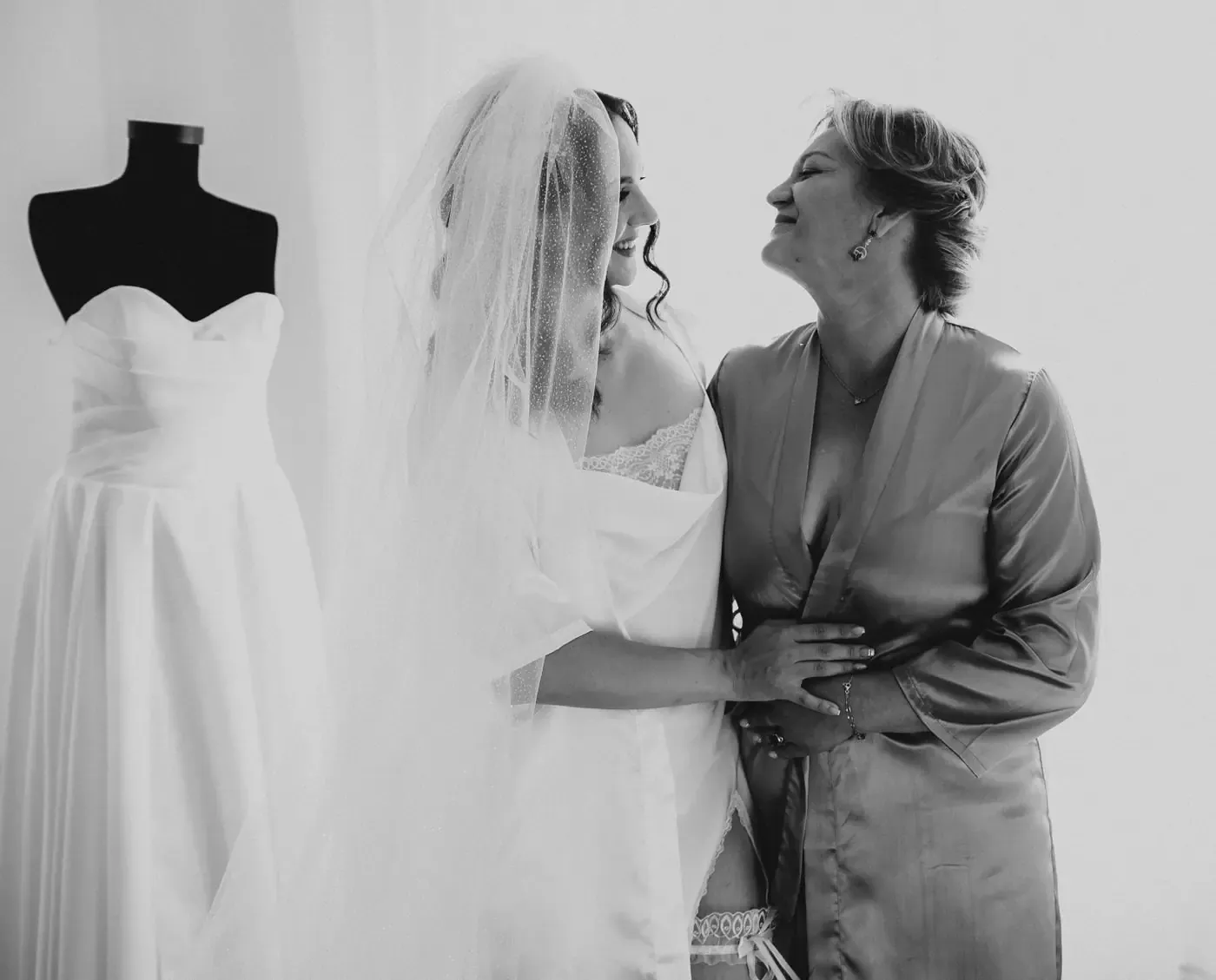Bride in wedding attire joyfully embraces her mother indoors, capturing a special moment.