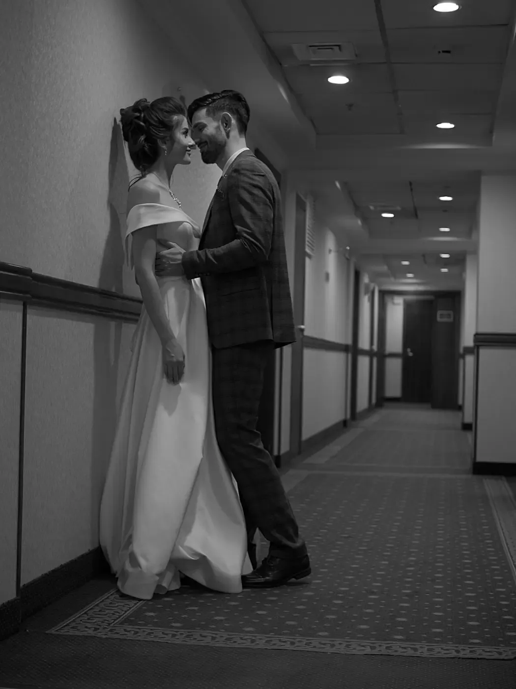 A couple in wedding clothes standing in a hallway, in black and white.