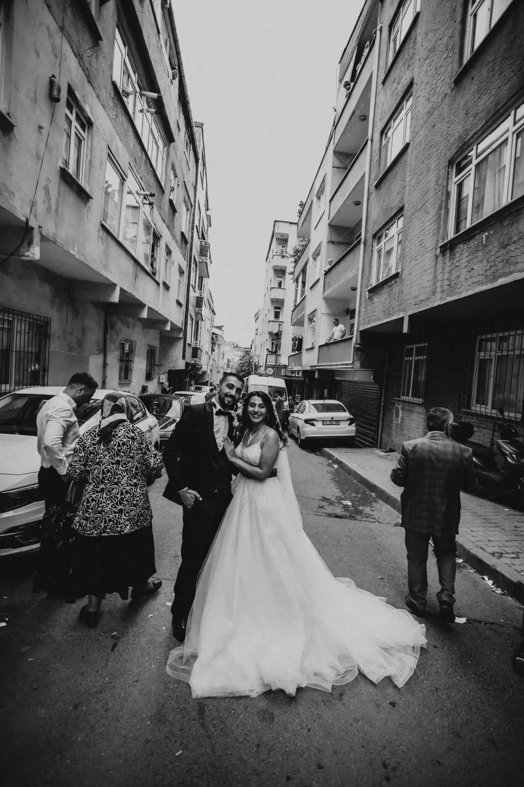 A newlywed couple standing on a city street between tall buildings, in black and white.