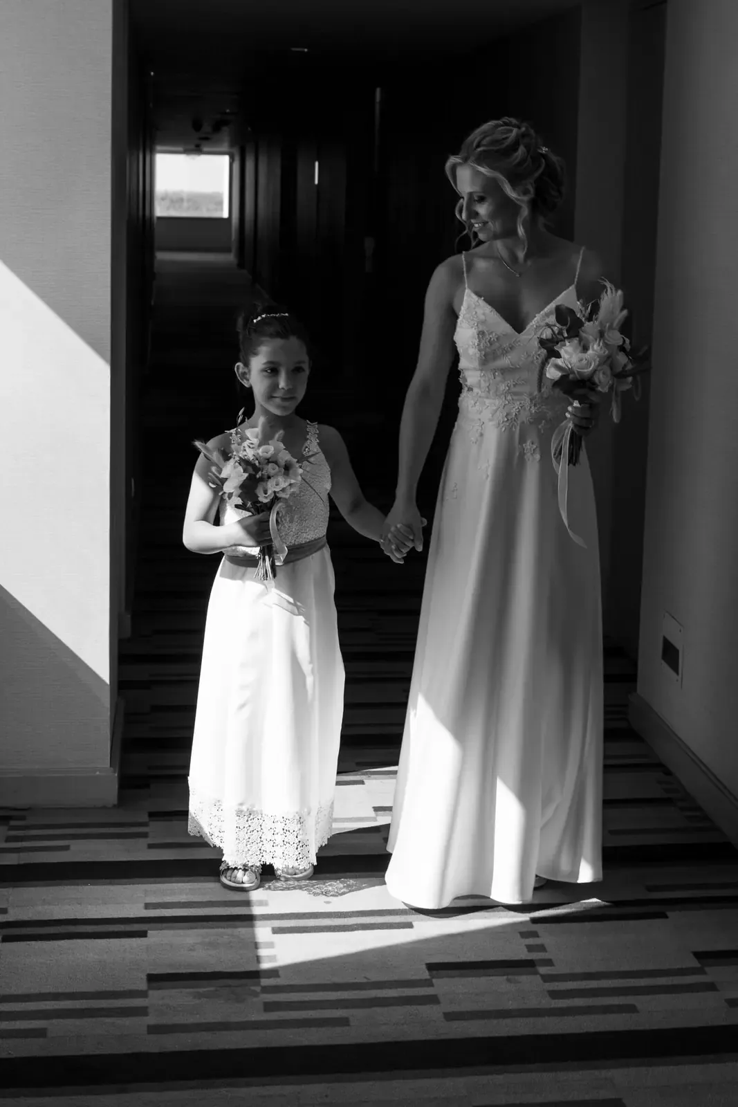 A bride and a small girl in white dresses holding flowers, in black and white.