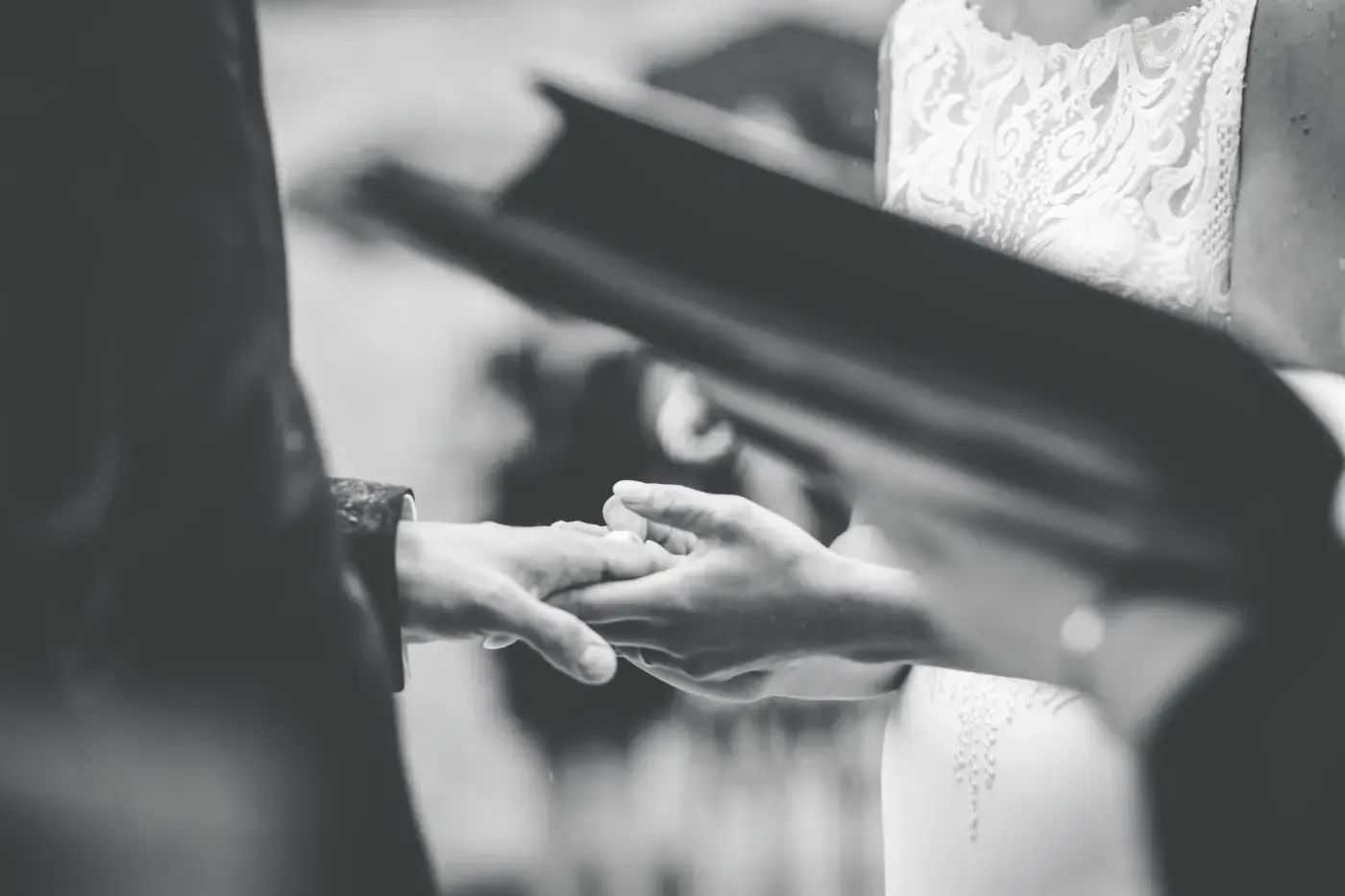 A bride and groom exchanging rings during the ceremony, in black and white.