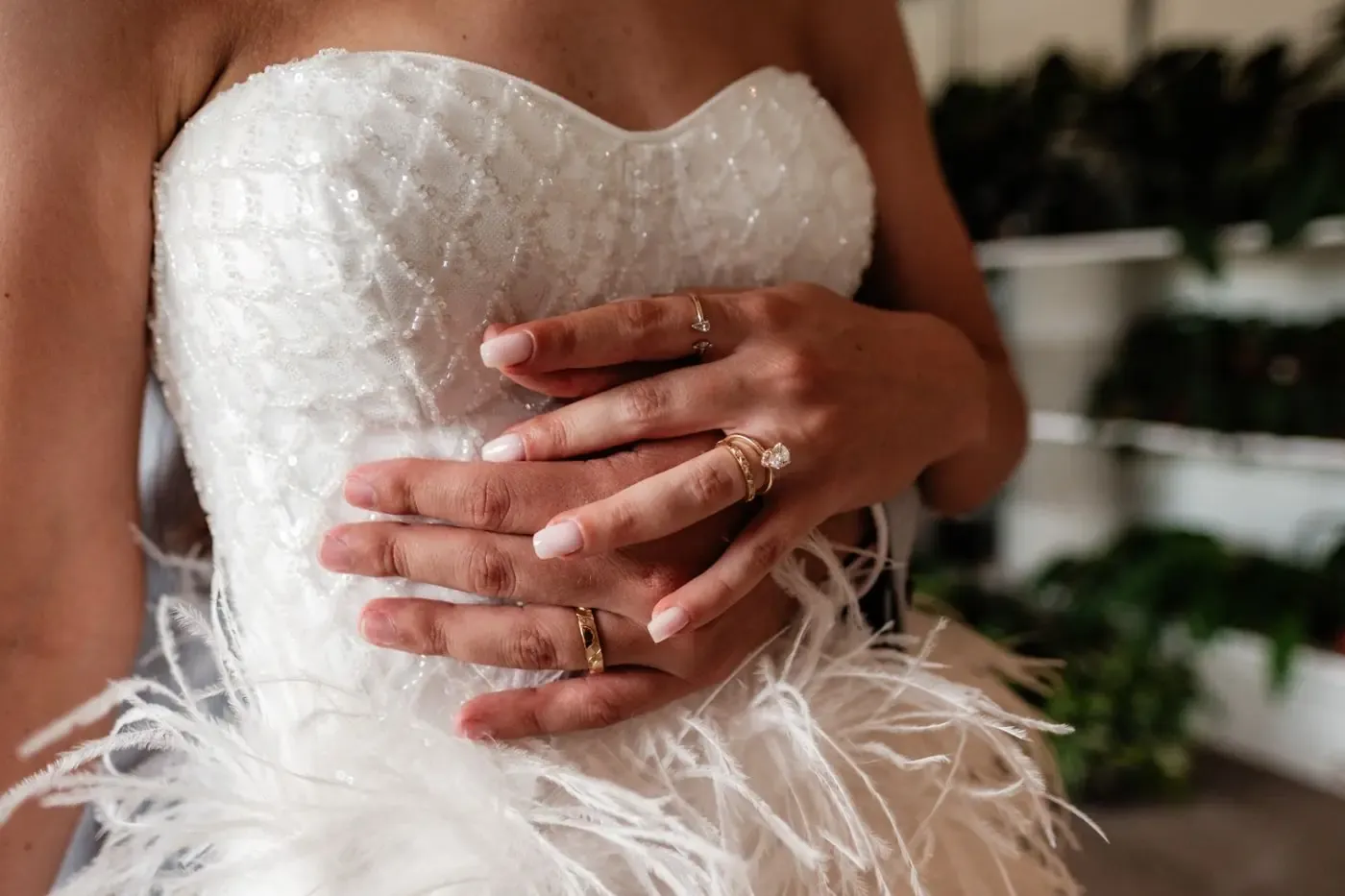 Close-up of hands on an embellished bridal gown with feather accents, showcasing elegant rings.