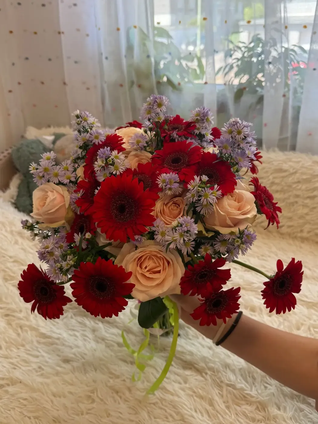 A beautifully arranged bouquet of red daisies, pale roses, and purple asters held indoors.
